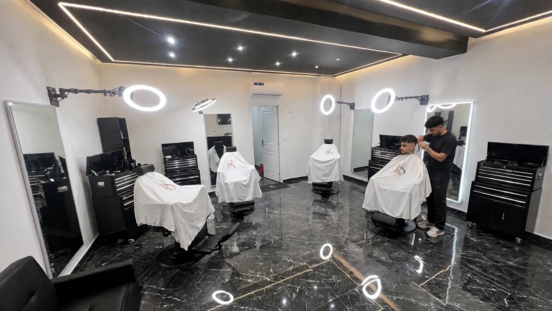 Un coiffeur réalise un dégradé dans le salon RS CUT'Z, sol en marbre noir et néons circulaires